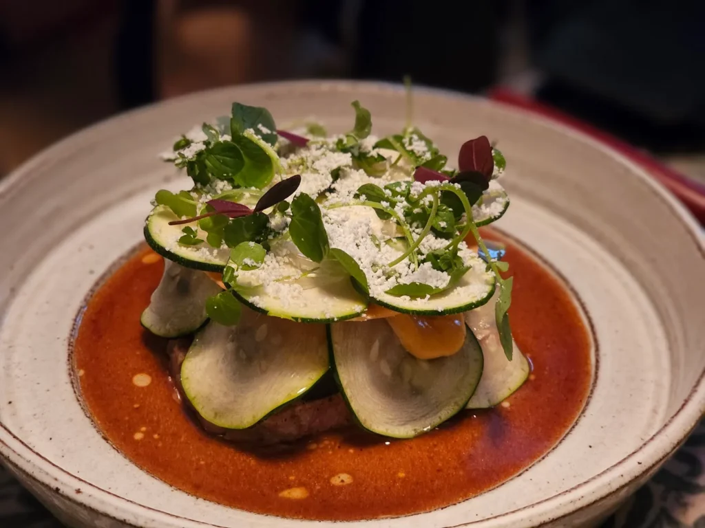 Kötträtt toppad med tunt skivad zucchini och örter